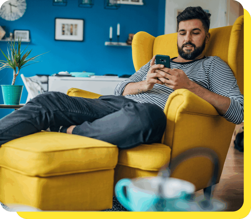 Man relaxing on a chair while using his phone, enjoying the stability of a fixed rate savings account.