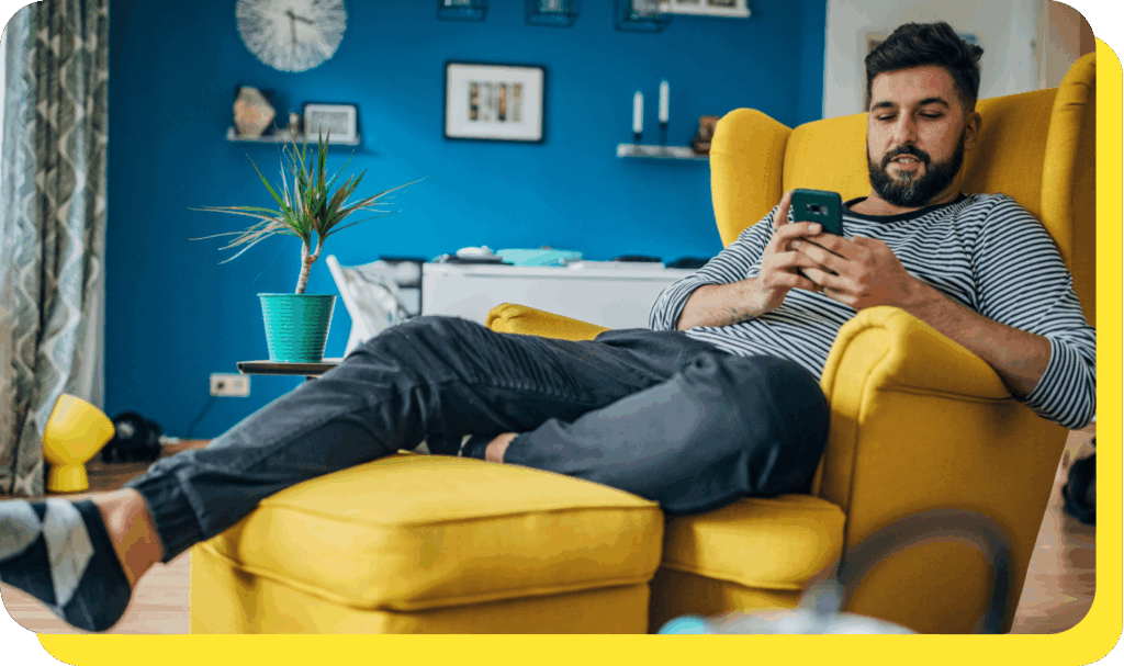 Man relaxing on a chair while using his phone, enjoying the stability of a fixed rate savings account.
