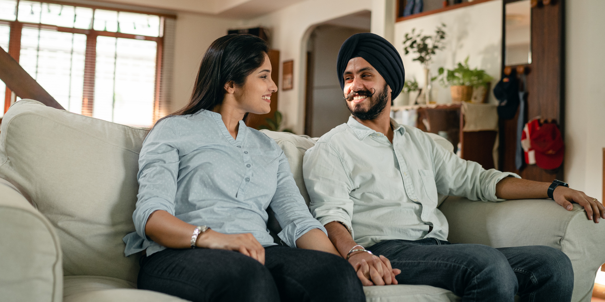 Couple sat on the sofa smiling while holding hands