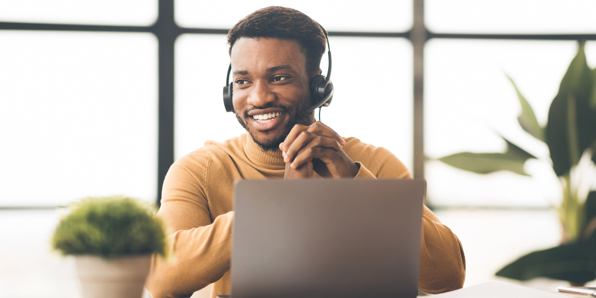 Man using laptop and speaking into headset with hands held together