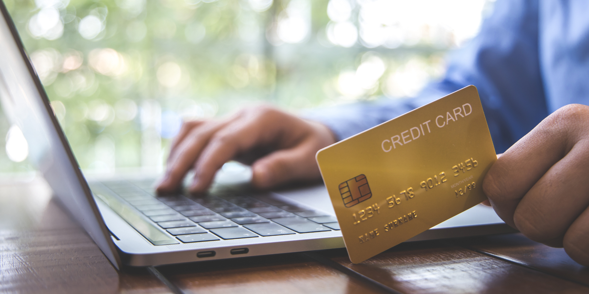 Close up of a hand holding a credit card while the other hand types on a laptop