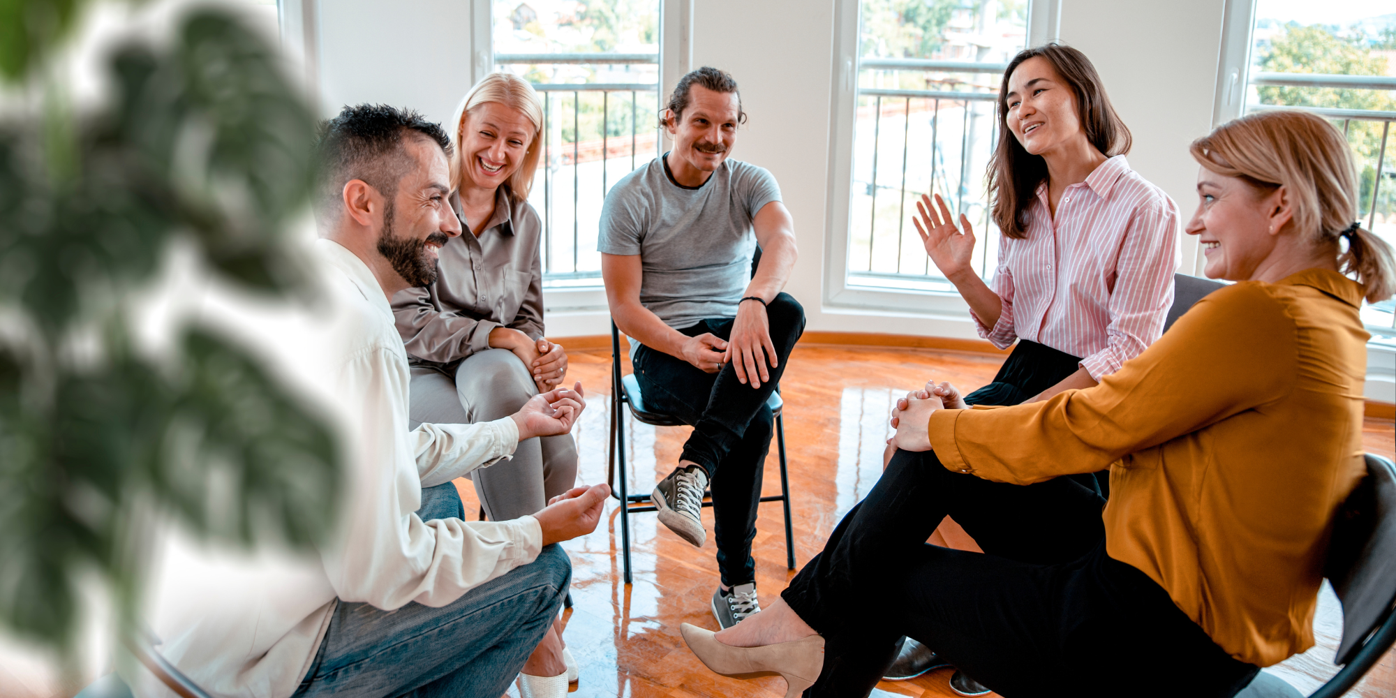 Support group of five people sat in a circle smiling and talking.