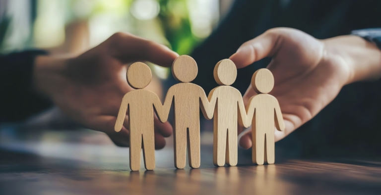 A pair of hands protecting a set of wooden people to represent employer provision of wellbeing schemes