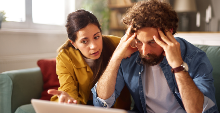Woman helping a stressed man sitting at a laptop.